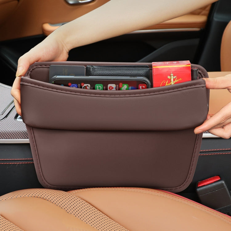 Brown car seat gap storage organizer pocket held by hands, open top with small items.