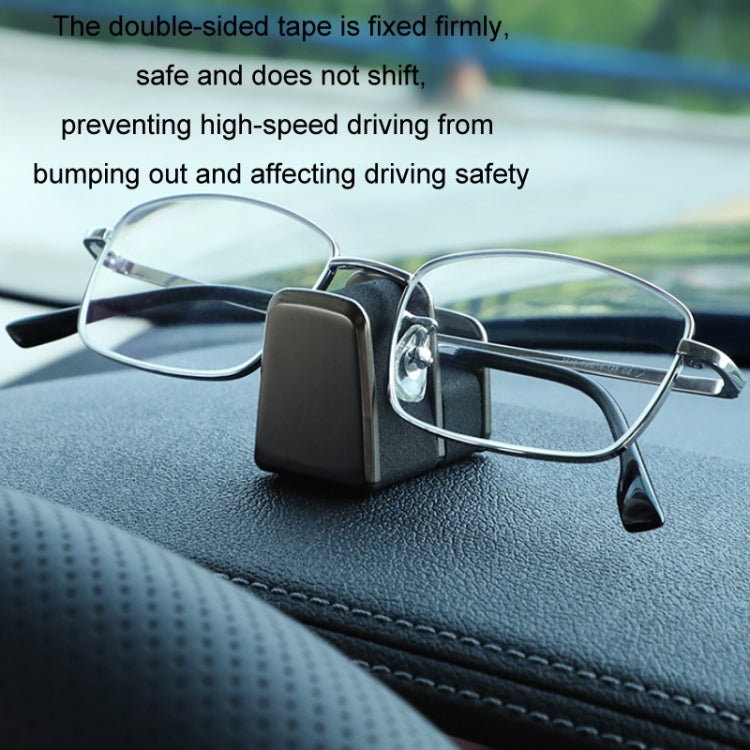 Car dashboard eyeglass holder with black case securing wire-framed glasses close-up