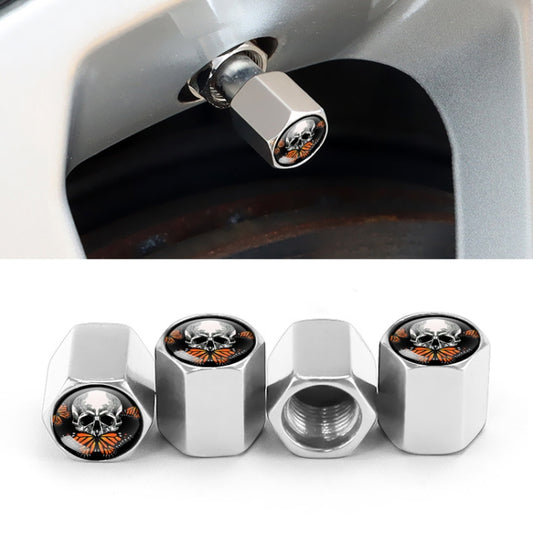 Silver metal tire valve caps with skull emblem, shown installed on a car wheel valve.