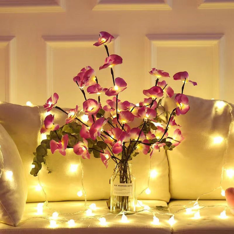 Pink butterfly orchid LED branch lamp in a vase with warm string lights