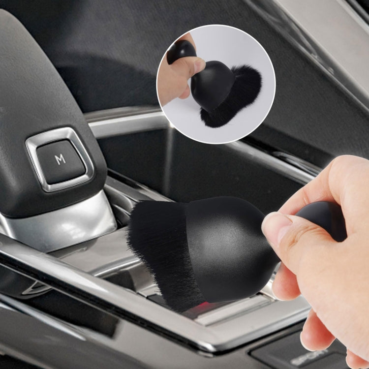 Black car interior cleaning brush with soft bristles held by hand near console