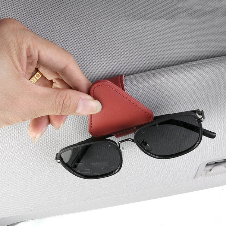 Red triangular storage clip holding black sunglasses on a car sun visor.