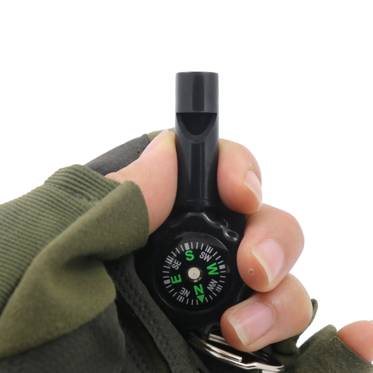 Black whistle compass with green compass dial and key ring, held in a hand