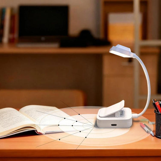 White clip-on LED reading lamp with curved neck over open book on desk