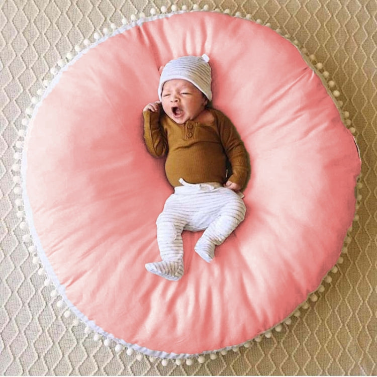 Pink round baby bean bag chair with white pom-pom trim and padded center