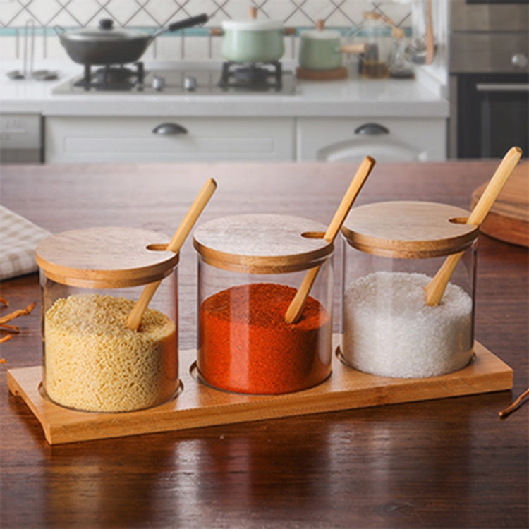 Three clear glass jars with bamboo lids and wooden spoons on a wooden tray with different refills