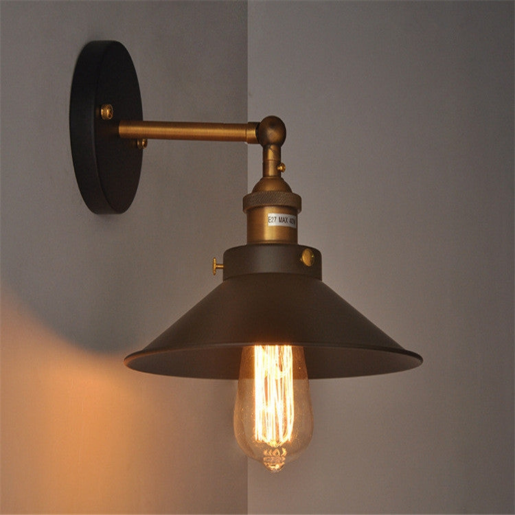 Retro wall sconce with black backplate and brass arm, bell shade and glowing exposed bulb