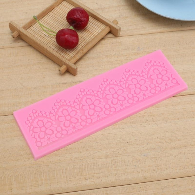 Pink lace silicone mould strip with repeating floral lace pattern on a wooden board