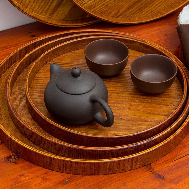 Round solid wood tea tray with dark teapot and two cups, nested top view
