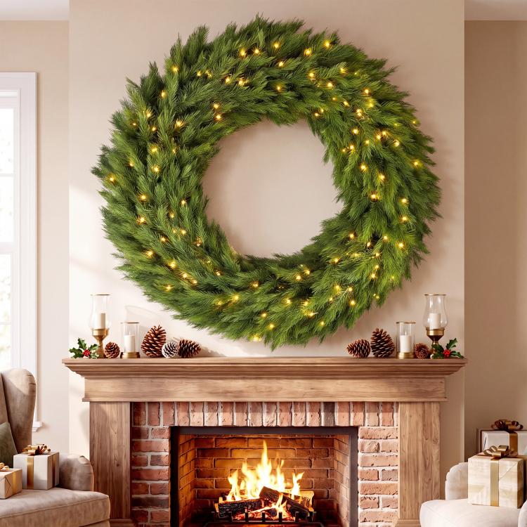 Pre-lit green evergreen wreath with warm LED lights hanging above a fireplace mantel.