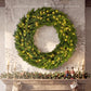 Green artificial Christmas wreath with warm LED lights displayed on a mantel against stone.
