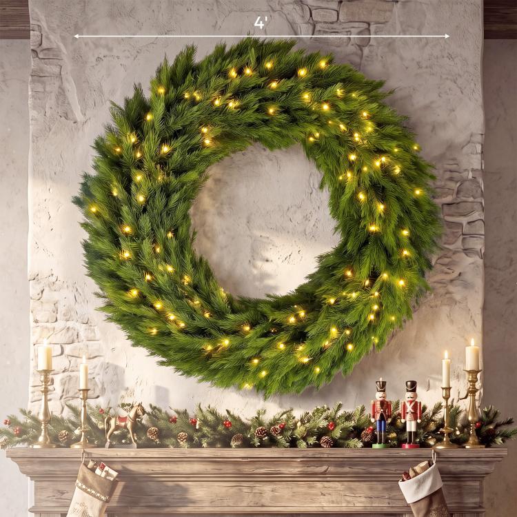 Green artificial Christmas wreath with warm LED lights displayed on a mantel against stone.