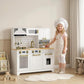 Child wearing chef hat next to white kids play kitchen with gold faucet and stove