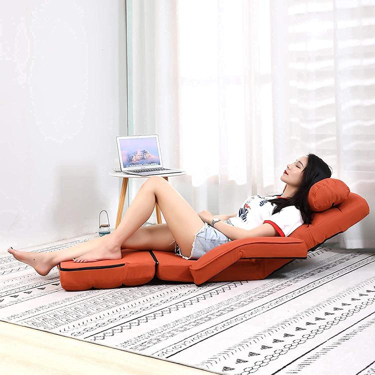 Orange reclining floor chair with attached head pillow, stretched leg rest, and cushioned seat