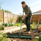 Green lawn leveling rake being used in a garden bed, held by a gardener