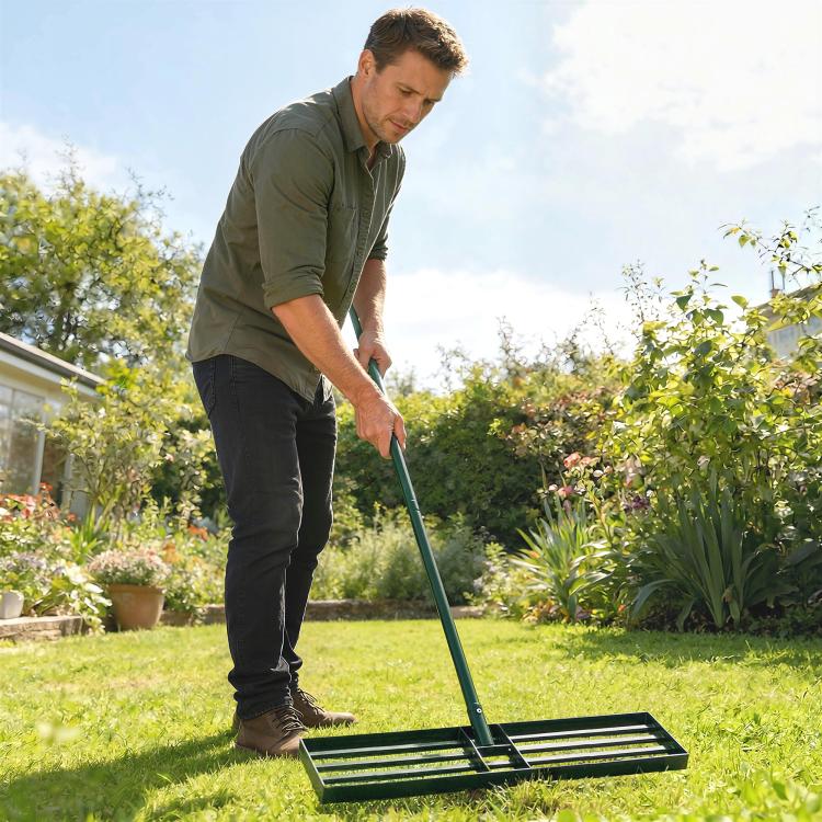 Lawn leveling rake with ridged base on grass, held by a person outdoors