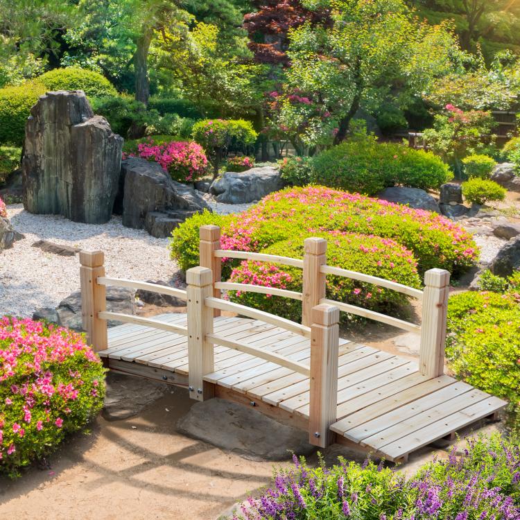 Wooden garden bridge with railings over a pond with landscaped edges
