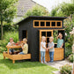 Black wooden kids playhouse with open front door and attached picnic table and bench