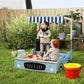 Blue kids wooden sandbox with striped canopy and bench seats, with toy sand tools