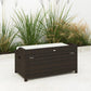 Outdoor wicker storage bench angled view, dark brown woven frame with light cream cushion