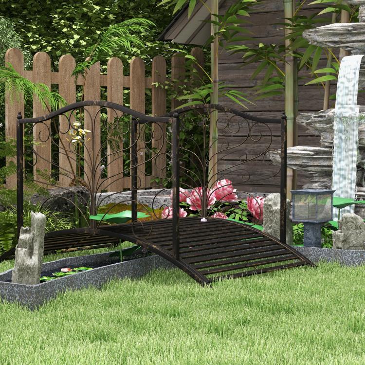 Dark bronze arched garden bridge with scroll side rails on lawn and stone border.