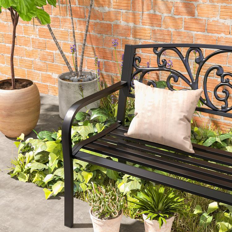 Black decorative patio bench with scrollwork back, slatted seat, and light throw cushions