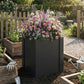 Black square raised garden bed planter box filled with pink and purple flowers