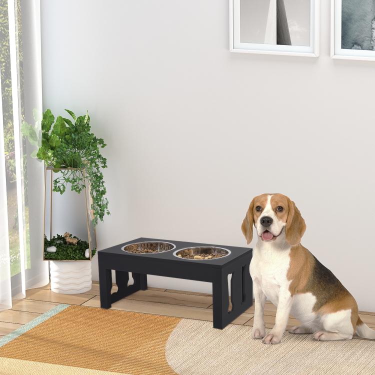 Black raised dog feeding station with two stainless-steel bowls; dog sitting nearby