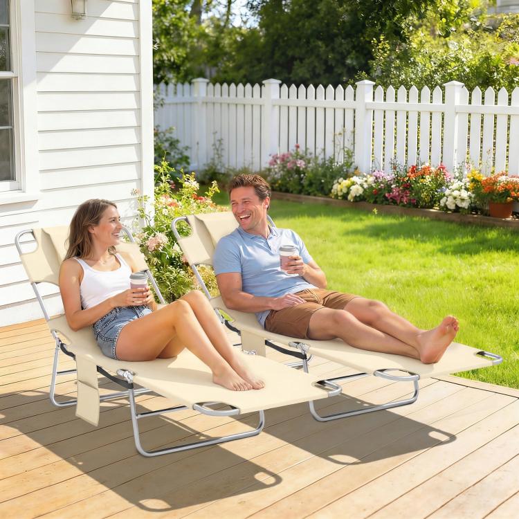 Two beige tanning chairs with face pillows, reclining outdoors on a wooden deck