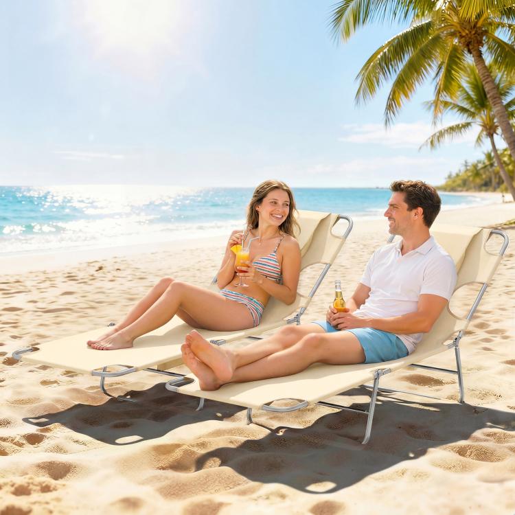 Two beige reclining tanning chaise lounges with face pillows on a sandy beach