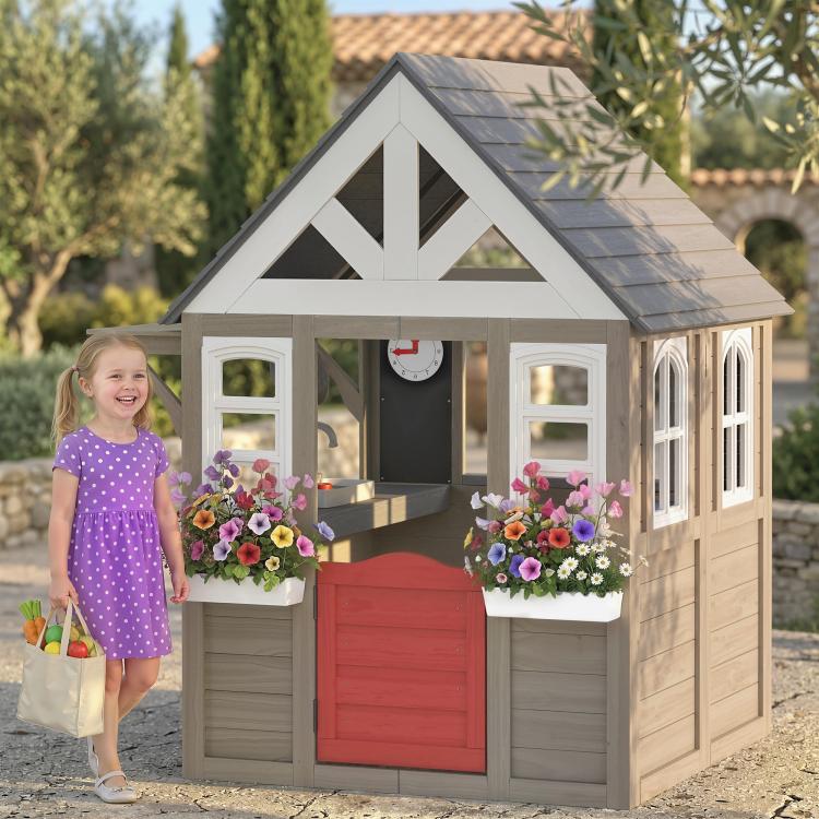 Gray wooden outdoor playhouse with dark roof, front half-door, and flower planters