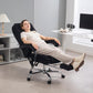 Black reclining massage office chair with footrest, shown in use in a home office.