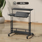 Black standing desk with tilting tabletop and keyboard tray on caster wheels, lower shelf.