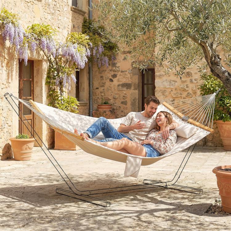 Cream two-person outdoor hammock with pillow and spreader bars between posts