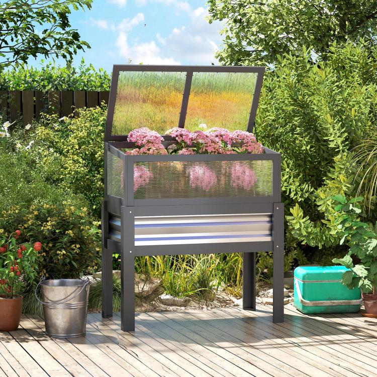 Gray raised planter box with mini greenhouse cover and pink flowers in garden