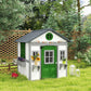 White wooden kids playhouse with green door and side windows, rooftop overhang and planters