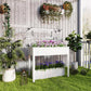 White raised garden bed with clear greenhouse cover holding rows of flowering plants
