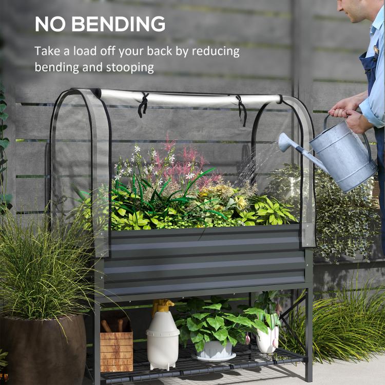 Dark gray raised garden bed with clear cover and person watering plants from side