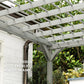 Gray pergola corner with cross-braced beams and slatted roof above plants
