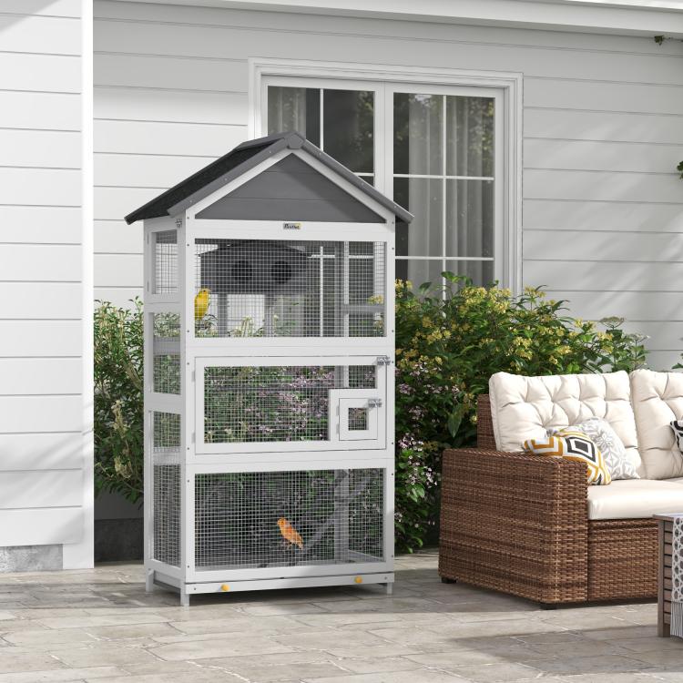 Gray wooden bird aviary with black roof and wire mesh enclosure on patio