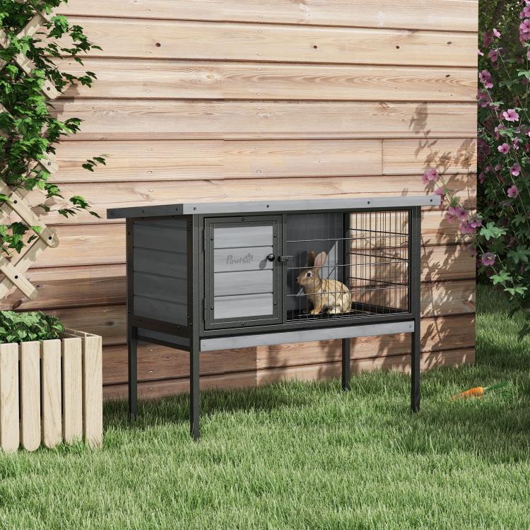 Gray elevated wooden rabbit hutch with open front door, rabbit resting on wire floor