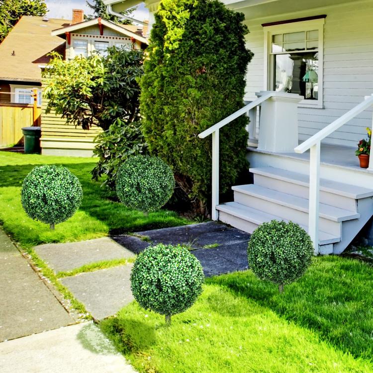 Artificial boxwood ball topiary trees set in an outdoor garden with ground stakes