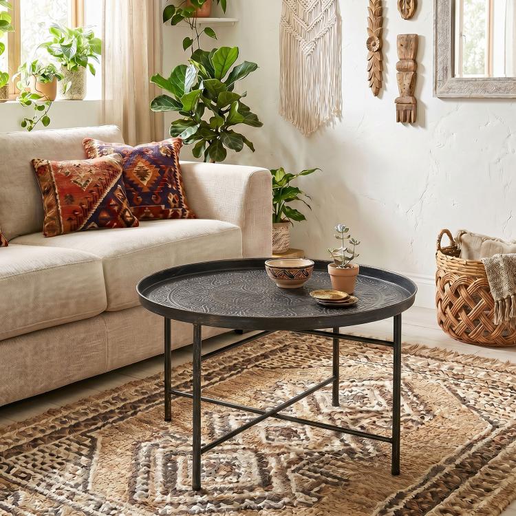 Round hammered-tray coffee table with dark metal legs and X-shaped support frame