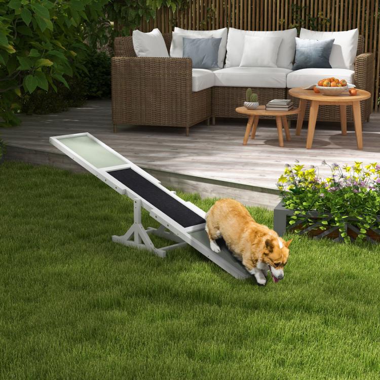White wooden dog agility seesaw with green ramps and black contact zone, dog using it