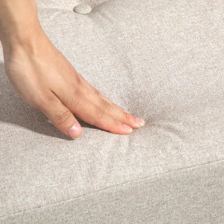 Beige upholstered floor sofa cushion with stitched seam, hand smoothing fabric