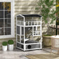 Light gray wooden cat house with dark roof and side entrance opening, outdoors