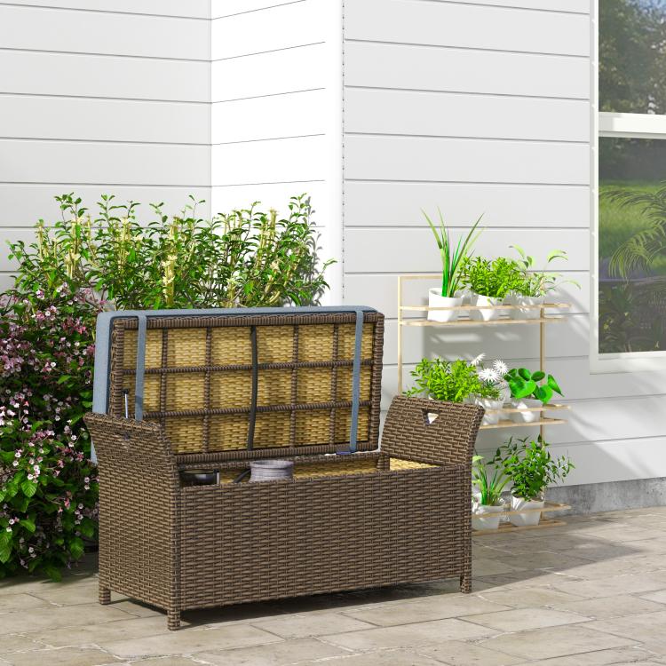 Outdoor wicker storage bench with dark blue cushion, on patio with plants.