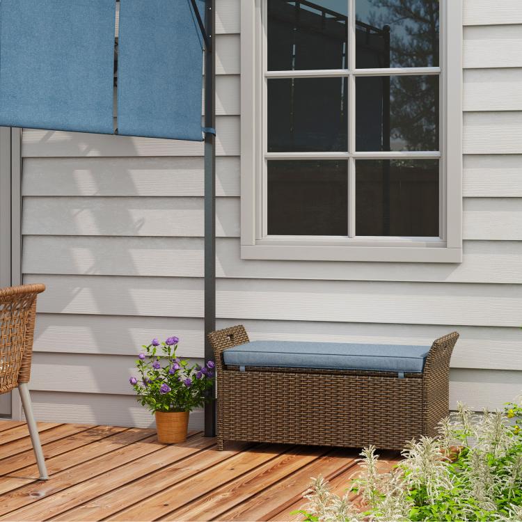 Outdoor wicker storage bench with dark blue cushion, on wooden deck.