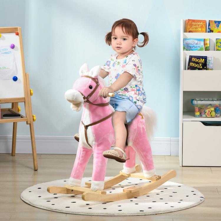 Pink plush rocking horse ride-on with child seated, wooden rocker base and bridle
