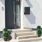Artificial boxwood ball topiary trees in black pots with green pom-pom foliage on steps